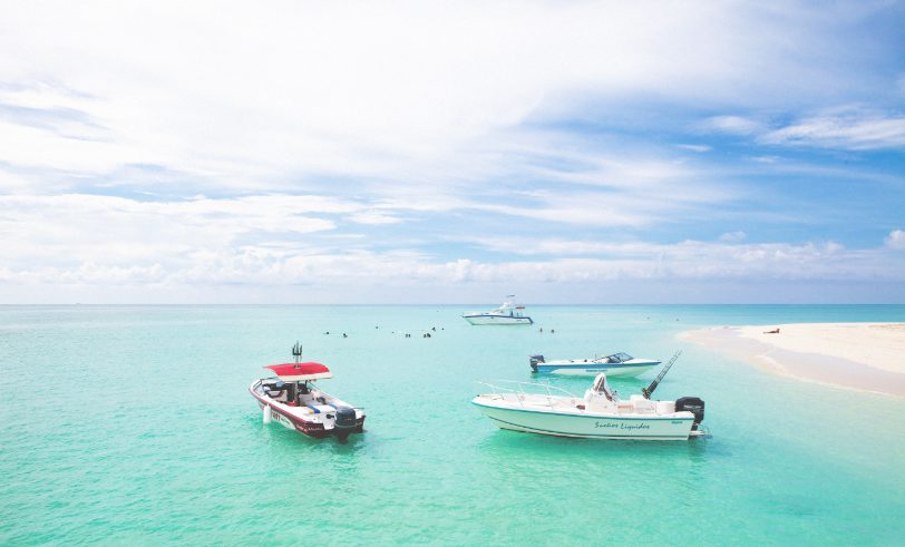 The Strand Turks and Caicos - group of boats on aqua blue Caribbean ocean with beachgoers in the background